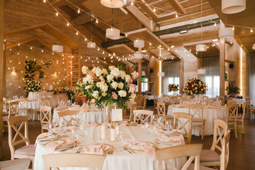Fototapeta na wymiar Coziness and style. Modern event design. Table setting at wedding reception. Floral compositions with beautiful flowers and greenery, candles, laying and plates on decorated table.
