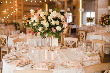 Coziness and style. Modern event design. Table setting at wedding reception. Floral compositions with beautiful flowers and greenery, candles, laying and plates on decorated table.