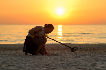 Man use metal detector on the beach in sun set