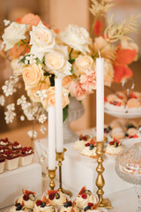 Candy bar with tasty desserts and appetizers at wedding reception. Decorated with flower compositions and candles. Sweet food, dessert, buffet, catering table, restaurant.