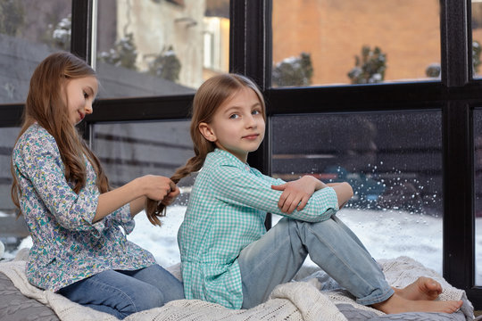 The image of two cute little sisters sitting on windowsill in peace and quiet