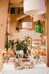 Candy bar with tasty desserts and appetizers at wedding reception. Decorated with flower compositions and candles. Sweet food, dessert, buffet, catering table, restaurant.