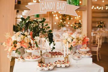 Candy bar with tasty desserts and appetizers at wedding reception. Decorated with flower compositions and candles. Sweet food, dessert, buffet, catering table, restaurant.