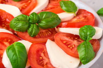 Italian caprese salad with sliced tomatoes, mozzarella cheese, basil, olive oil in a plate on gray concrete background