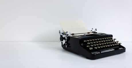 Old retro vintage black typewriter in black laid on white desk in front of white wall with paper and copy space