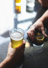 Hands holding a glass of beer at a table in a bar