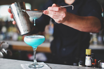 bartender pouring a cocktail into glass