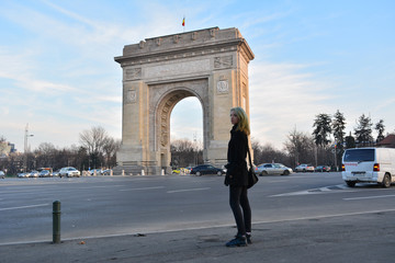 A blonde model with mermaid hair looking at the Arc of Triumph in Bucharest, Romania