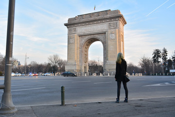 A blonde model with mermaid hair looking at the Arc of Triumph in Bucharest, Romania - obrazy, fototapety, plakaty