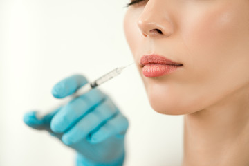 Close up of medical doctor in blue gloves injecting woman in the lips with a suringe