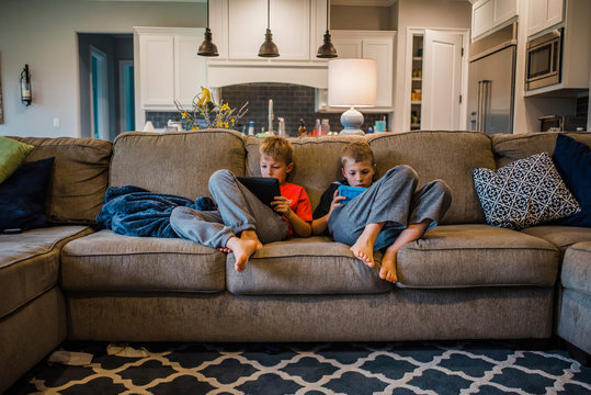 Brothers using tablet computers while relaxing on sofa at home