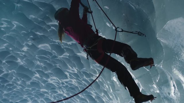 Low angle view of climber in ice cave using rope and hooks / Palmer, Alaska, United States