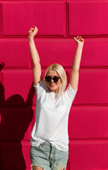 Excited casual woman in sunglasses against red wall 