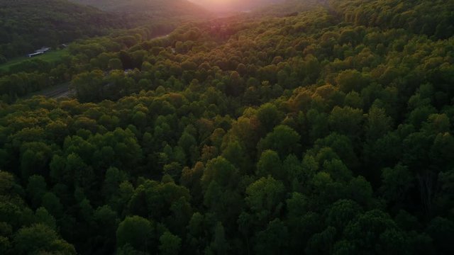 Aerial flyover view of distant cars driving on road near forest at sunset / Susquehanna, Pennsylvania, United States