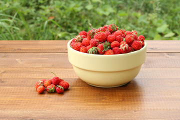 Ripe red pine strawberry in yellow bowl on brown wooden table against green grass background