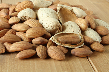 Pile of peeled raw almonds and raw almonds with shells on wooden table. Closeup