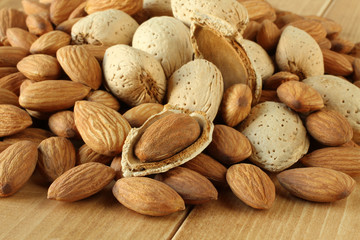 Pile of peeled raw almonds and raw almonds with shells on wooden table. Closeup