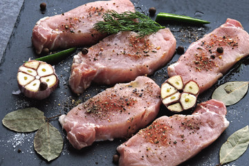 Raw pork steaks with garlic and spices on a stone board. The concept of cooking meat. Keto diet. Paleo diet. Pegan diet.