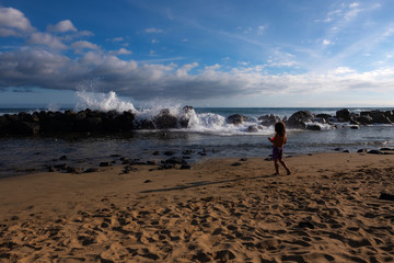 Silhouette of young girl watching the waves breaking at a mole at the beach of Maspalomas, Gran Canaria