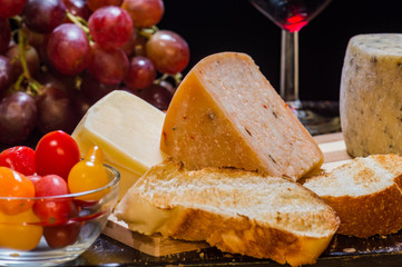 Mexican artisanal cheese and heirloom tomatoes, wine and grapes on black background