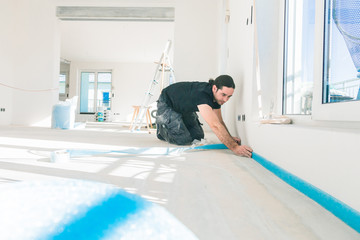 Workers in a flat work on a floor. glue edge insulation strip. balance the floor.