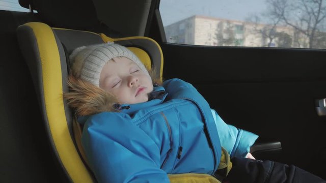 Toddler boy sleeping in child safety seat in car.