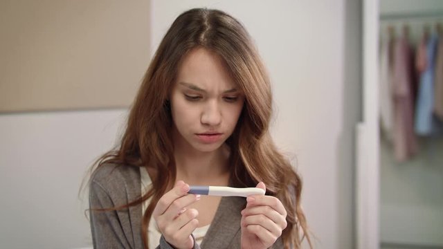 Worried woman waiting pregnant test results. Girl looking at pregnancy test
