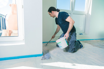 House under construction. Worker puts primer on concrete floor.