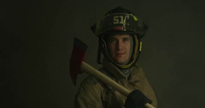 Fire fighter holding fireman axe looking stoic towards camera as smoke and red lights flash