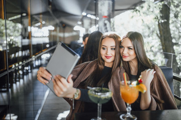 Two beautiful friends make selfie with hookah on the summer terrace of a modern cafe.