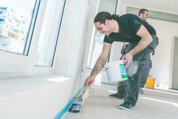 House under construction. Worker puts primer with roller on concrete floor.