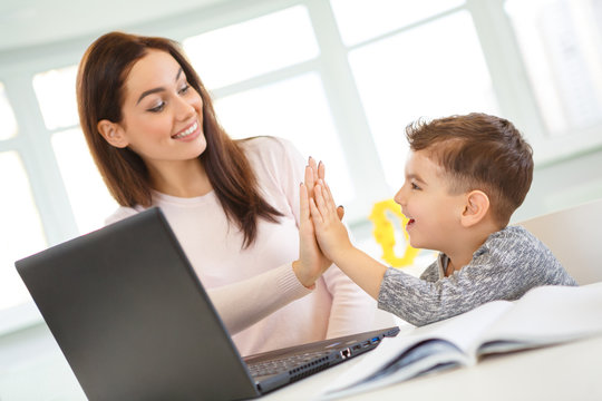 Beautiful teacher helping her little student with studying on the laptop