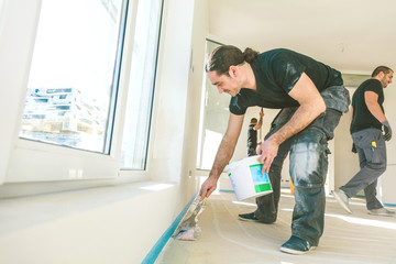 House under construction. Worker puts primer with roller on concrete floor.