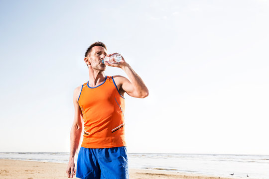 Athlete drinking from bottle on the beach