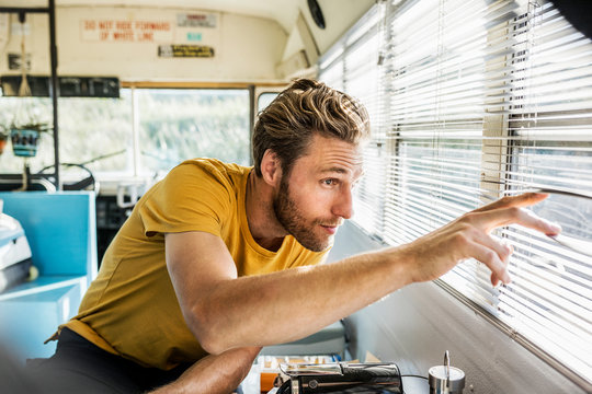 Young man looking through window blinds while sitting in bus