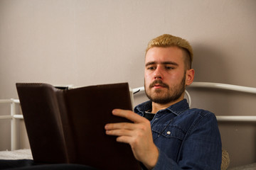 Stylish bearded man is reading book. Calm hipster is spending time on couch with book