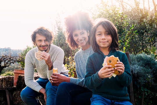 Happy family siting in garden, taking a break, eating sandwiches