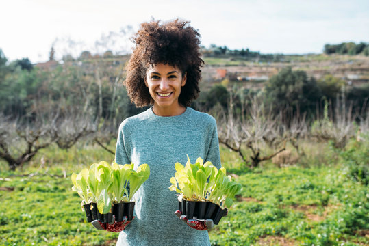 Smiling woman holding lettuce seedlings in a vegetable garden