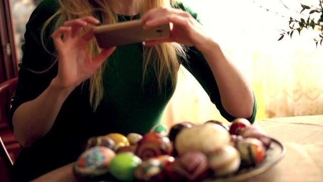 Beautiful woman taking photo with cellphone of easter egg plate, super slow motion