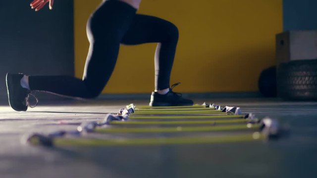 close-up, female legs in black leggings and sneakers. woman performs exercises with an athlete's foot ladder, jumps , training on agility ladder on floor, in gym. Fitness class cardio workout