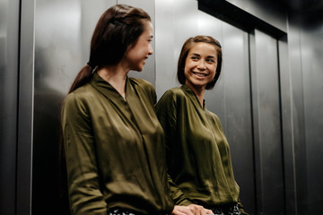 Smiling young woman looking in mirror in elevator