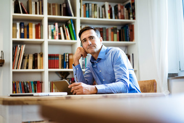 Businessman with tablet sitting at table with bookshelf in background