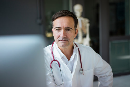 Doctor in medical practice looking at computer with skeleton in background