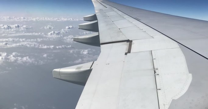 Aerial view of cirrus and cumulus clouds and aircraft engine and wing through airplanes windows which fly over thick layer of cloud and background of clear blue skyline.