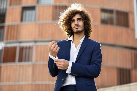 Portrait of young fashionable businessman with curly hair wearing blue suit buttoning cuff link