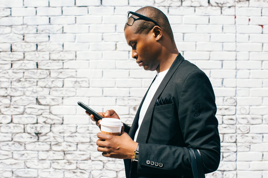 Mid adult man in front of white brick wall, holding smartphone and cup of coffee