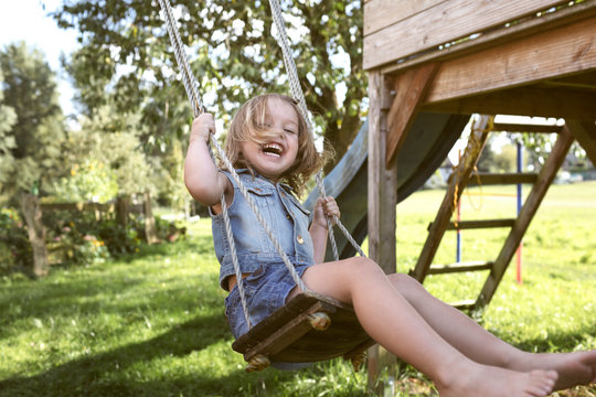 Laughing little girl sitting on swing in the garden