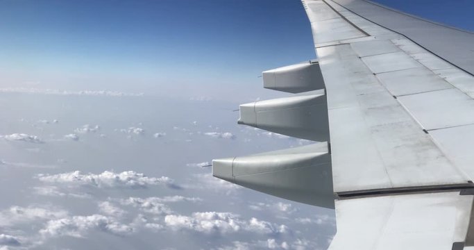 Aerial view of cirrus and cumulus clouds and aircraft engine and wing through airplanes windows which fly over thick layer of cloud and background of clear blue skyline.