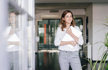 Businesswoman standing in office, holding laptop