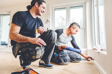 Mann mit der Kleberspritze befestigt die Sockelleiste an einer Baustelle. Parkettboden verlegen.